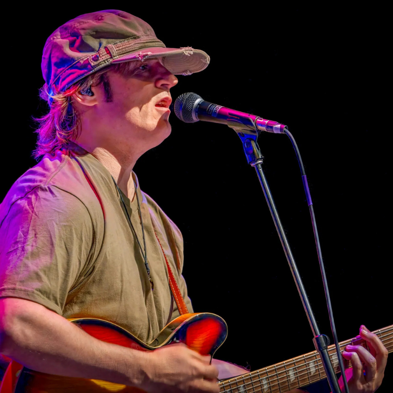 Sixtiesmania® 60s tribute band guitarist and vocalist singing into a microphone while playing electric guitar during a live rock performance.